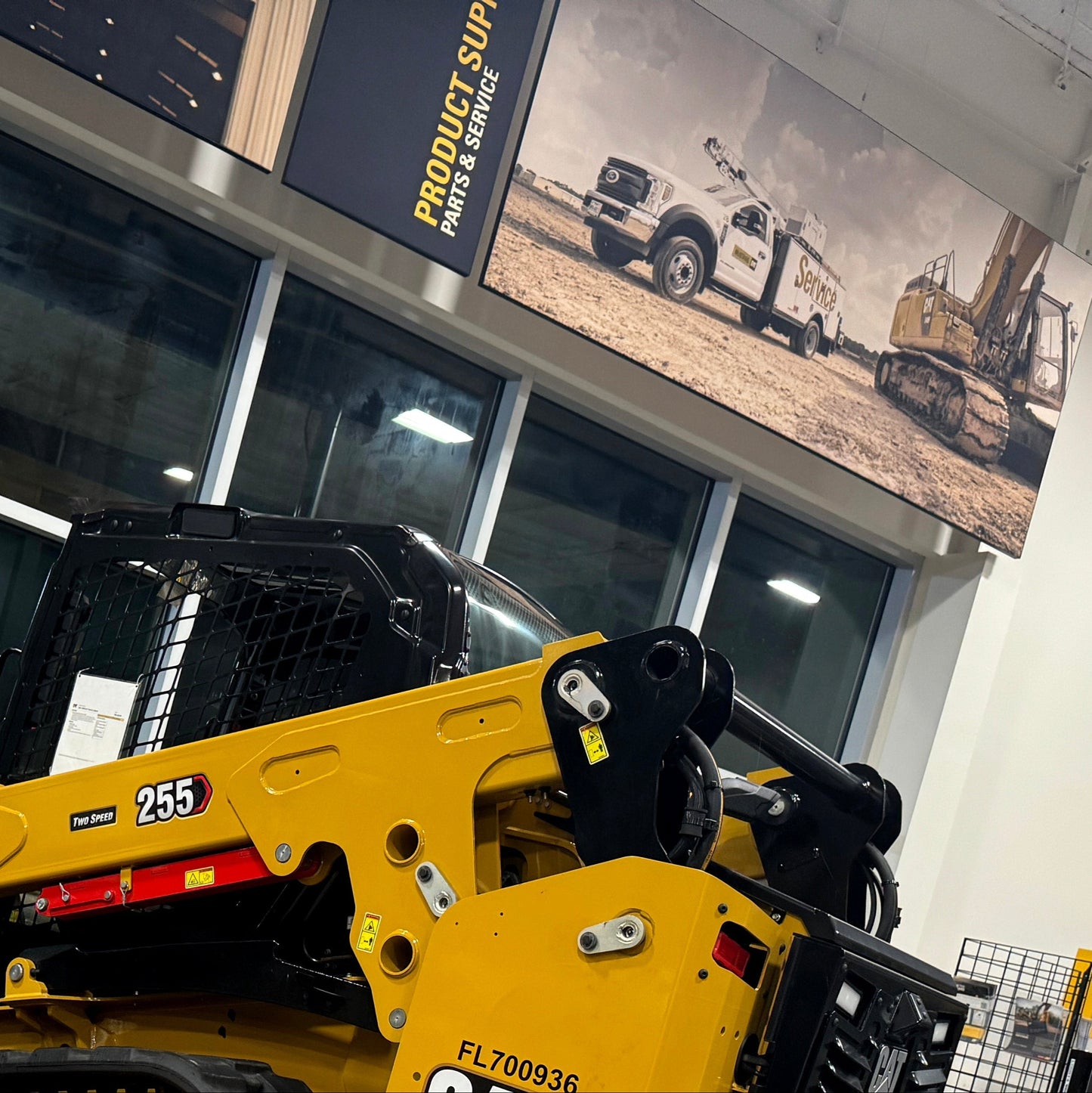 Yellow construction vehicle in a showroom with a large banner in the background.