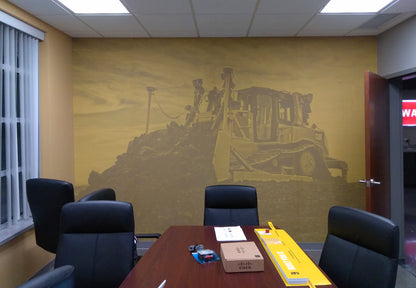 A large wall mural in an office setting depicting construction equipment, applied to the wall behind a meeting room table.